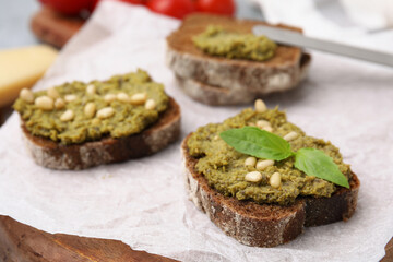 Tasty bruschettas with pesto sauce, nuts and fresh basil on wooden board, closeup