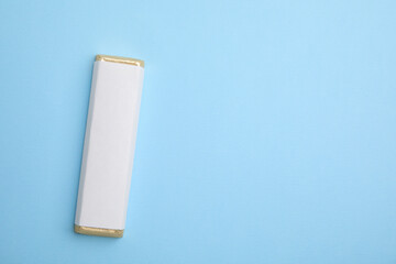 Tasty chocolate bar in package on light blue background, top view. Space for text