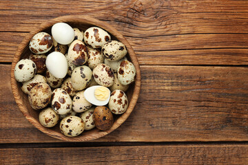 Unpeeled and peeled hard boiled quail eggs in bowl on wooden table, top view. Space for text