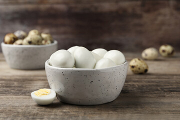 Many peeled hard boiled quail eggs in bowl on wooden table, closeup