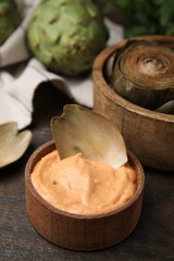 Delicious cooked artichoke with tasty sauce on wooden table, closeup