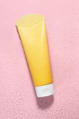 Tube of facial cleanser in water against pink background, top view