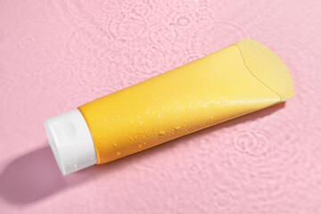 Tube of face cleansing product in water against pink background