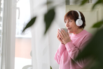 Senior lady in pink sweater finds joy in coffee and tunes - happiness at any age