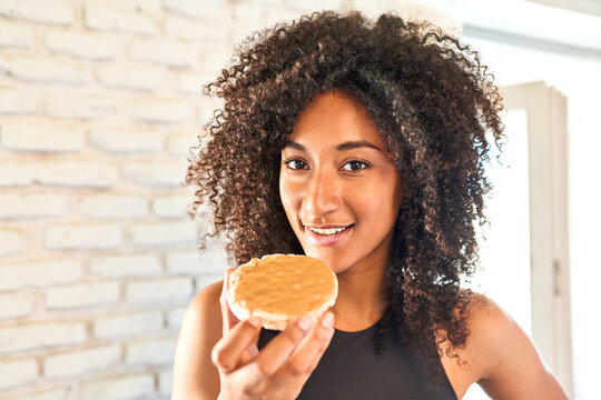 Health-conscious young woman in sportswear enjoys a nourishing rice cake with peanut butter, embracing a healthy diet.