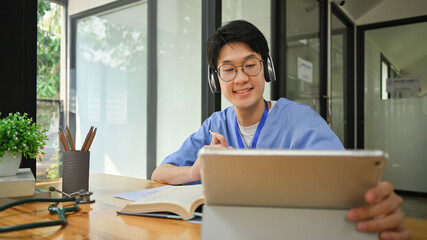 Medical student wearing headphone using digital tablet, preparing for university exams. Medical...