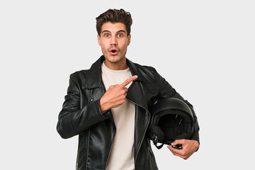 Young caucasian man holding a motrbike black helmet isolated pointing to the side