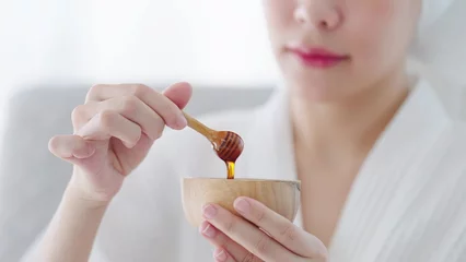 Keuken foto achterwand Spa Close up hand of woman holding wooden honey scoop dripping with pure honey in wooden bowl. Skincare spa relax concept