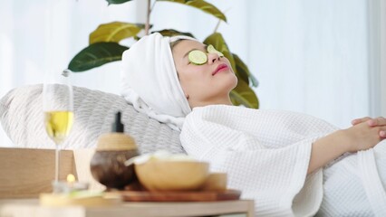 Beautiful woman wearing towel on head laying on spa bed feeling relax with cucumber slices on eyes...