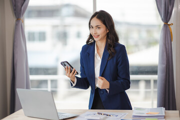 Obraz premium happy young woman excited at work Successful Asian businesswoman with laptop smartphone at work.