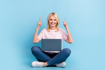 Full body portrait of cheerful nice person sit floor use netbook direct fingers up empty space isolated on blue color background