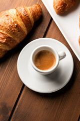 Tazzina di caffè espresso con cornetto su sfondo in legno, colazione italiana 