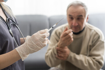 Doctor giving vaccination shot to elderly patient by syringe or injunction at home. concept of home...
