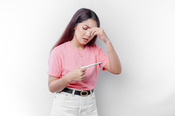 Unhappy woman wearing pink t-shirt looking at pregnancy test alone, confused young female shocked...