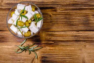 Chopped feta cheese, rosemary and olives in glass bowl on a wooden table. Top view