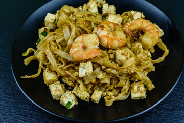 Black plate with pad thai on a slate board
