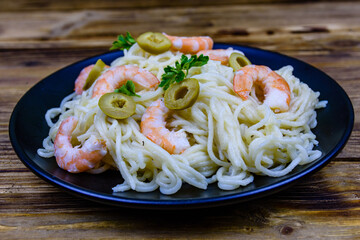 Italian pasta with shrimps and olives in a black plate