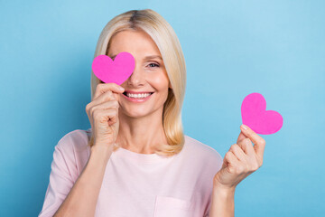 Photo of cheerful cute person toothy smile arms hold small heart cards cover one eye isolated on...