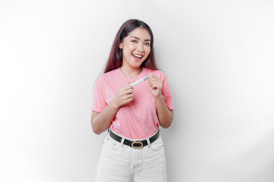 Happy young woman wearing pink t-shirt showing her pregnancy test and ultrasound picture, isolated on white background, pregnancy concept