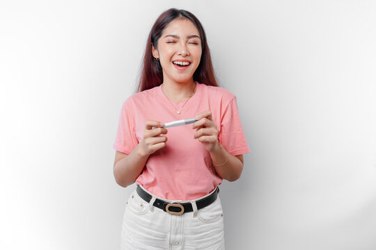 Happy young woman wearing pink t-shirt showing her pregnancy test and ultrasound picture, isolated on white background, pregnancy concept