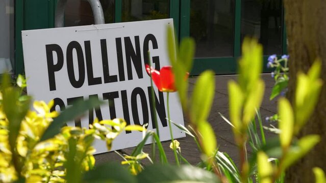 A polling station sign in front of flowers with a voter walking past