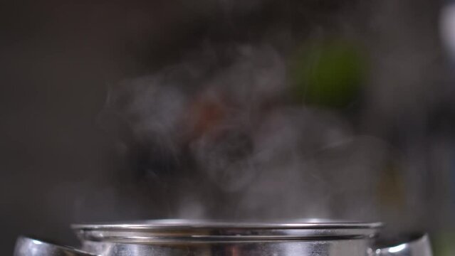 Close-up white evaporation out of saucepan in kitchen indoors. Closeup hot steam raising up in slow motion indoors
