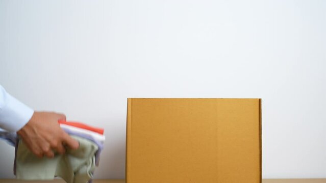 Donation, Charity, Volunteer, Giving and Delivery Concept. Hand holding Clothes into Donation box at home or office for support and help poor, refugee and homeless people. Copy space for text