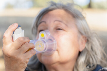 woman uses a nebulizer inhaler for the treatment of respiratory diseases. she is in the countryside breathing fresh air and enjoying the sun.