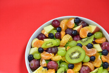 Healthy fresh fruit salad bowl on red background. Top view. Healthy food concept, healthy high vitamin fruit, mixed fruit background.