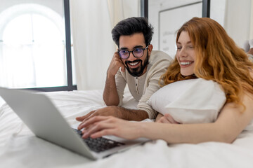 Wife and husband using laptop in bedroom, browsing internet together or watching movie.