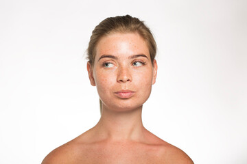 Obraz premium Pretty girl with freckles looks away with her hair tied up in front of the camera on a white background