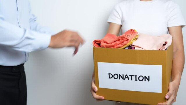 Donation, Charity, Volunteer, Giving and Delivery Concept. Hand holding Clothes into Donation box at home or office for support and help poor, refugee and homeless people. Copy space for text