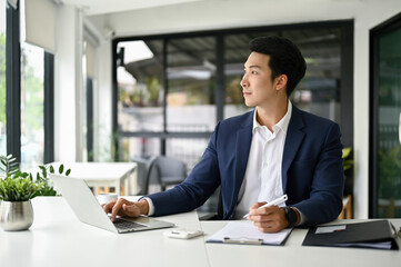 Fototapeta premium Handsome businessman sits at his office desk, looking out the window and daydreaming