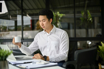 Naklejka na ściany i meble Focused Asian businessman reading business online documents on his laptop