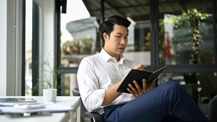 A businessman focuses on reading a book while sitting at his desk.