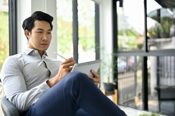 Handsome Asian businessman using his digital tablet at office lounge.