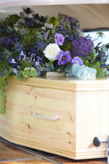 Close Up Of Plain Wooden Coffin With Floral Tributes In Back Of Hearse At Funeral
