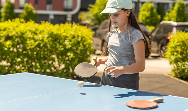 Young teenager girl playing ping pong. She holds a ball and a racket in her hands. Playing table tennis outdoors in the yard