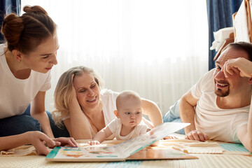 Parents together with their child play and study a children's book, lying on the floor in a bright children's room. Happy friendly family concept.