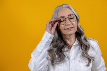 Intelligent senior woman in eyeglasses on yellow background