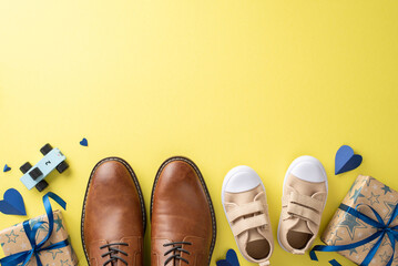 Father's Day celebration with dad and cute son. Top view of leather shoes, baby sneakers, hearts, car toy, and gift boxes on yellow background with room for text
