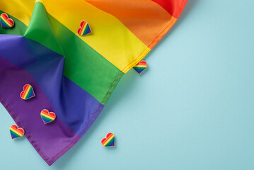 LGBTQ History Month concept. Top view flat lay of rainbow-themed parade accessories, symbolic flag, and pin badges on pastel blue background with empty space for text or ad