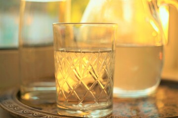 Glass of water and jug of water in a tray on the sunny windowsill.