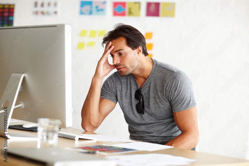 Aufkleber Suffering from writers block. A handsome man sitting at a desk and looking at a computer screen with head rested on his hand.