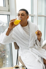 Good-looking young man in white robe having healthy breakfast