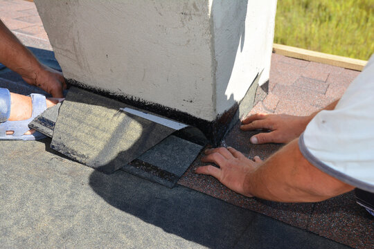 A close-up on a roofing construction, installation of asphalt shingles on roof sheathing around a house chimney using waterproofing corner flashing.  Roofing construction.