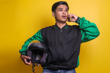 Asian online taxi driver motorbike wearing green jacket and holding helmet while having a phone...