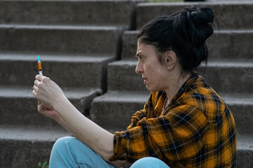 medicine. a woman addict with a cigarette in her hands sits on the steps. she holds in her hands a...
