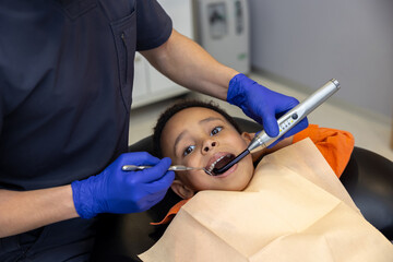 Dark-skinned boy looking scared while dentist treating his teeth