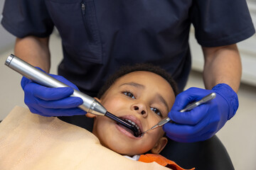 Dark-skinned boy looking scared while dentist treating his teeth
